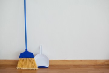 Dustpan and sweeping broom leaning against white wall