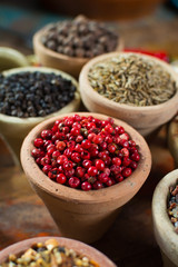 Variety of different spices with focus on pink Peruvian pepper, false pepper used in four peppers blends