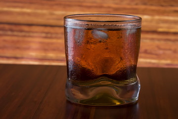 Glass of wiskey and ice on wooden background