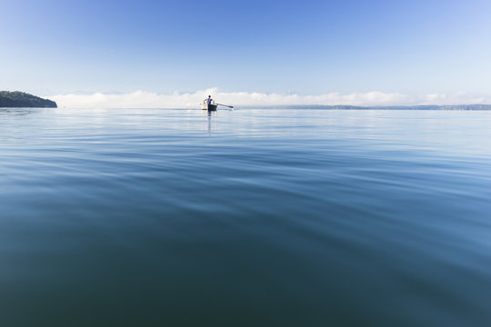 Man in a rowboat on lake Starnberg, the Alps and mount Zugspitze in early morning fog, Berg, Upper Bavaria, Germany