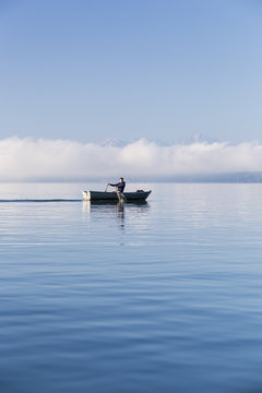 Man in a rowboat on lake Starnberg, the Alps and mount Zugspitze in early morning fog, Berg, Upper Bavaria, Germany