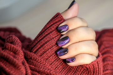 Beautiful nail polish in hand, purple nail art manicure, red background