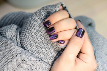 Beautiful nail polish in hand, purple nail art manicure, gray background