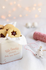 Christmas-shaped shortbread cookies packaged in a gift box. Candles and christmas lights in the background.