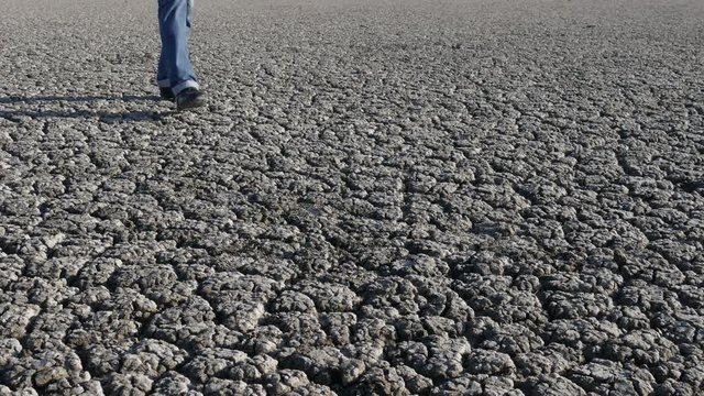Man in jeans and boots walking on dry cracked land after drought