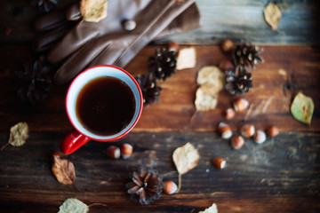 Hands in red knitted gloves holding a hot cup of coffee against yellow leaves background. Concept...