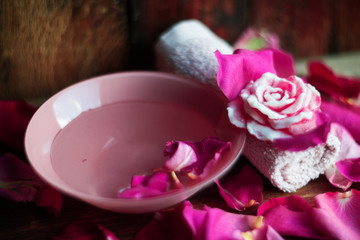Bowl with water and rose petals on wooden table