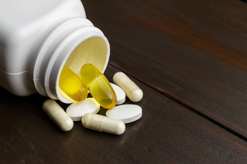 Yellow capsules of omega-3 in bottle, white capsules of glucosamine, white pills of calcium on wooden table
