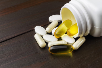 Yellow capsules of omega-3 in bottle, white capsules of glucosamine, white pills of calcium on wooden table