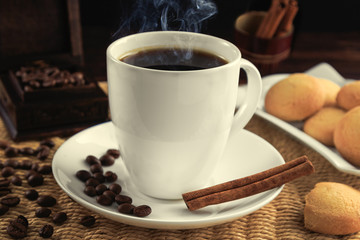Cup of black coffee and grains of coffee with cinnamon sticks and cookies.