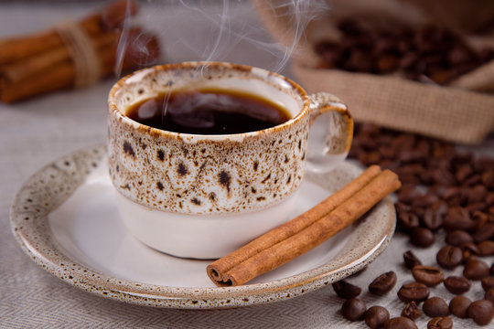 Cup of black coffee and grains of coffee with cinnamon sticks.