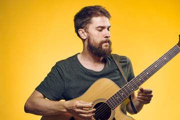 A man with a beard holds a guitar on a yellow background, musical instruments, a musician