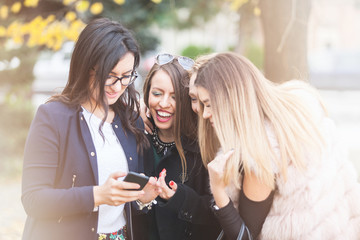 Group of four girl friends looking at phone on the selfie they where taking it. Friendship and city style