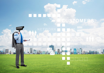 Camera headed man standing on green grass against modern cityscape
