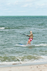 Extreme sport, with a young male riding a kiteboard being  pulled by a canopy fill with wind in rough, waters off, a tropical beach on the Gulf of Mexico, requiring strength, power and balance