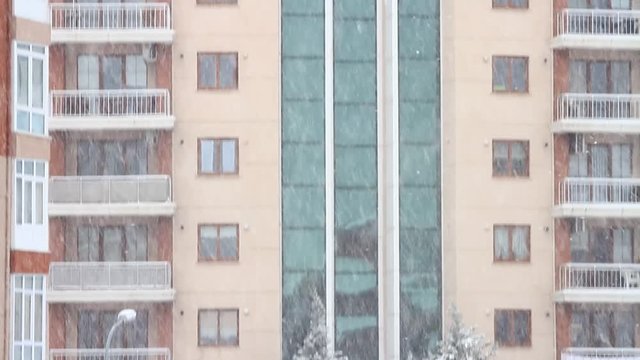 Snow falling in front of the multistored, stylish living block of flats. Tilt up
