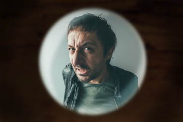 Angry man at the door viewed through spy hole