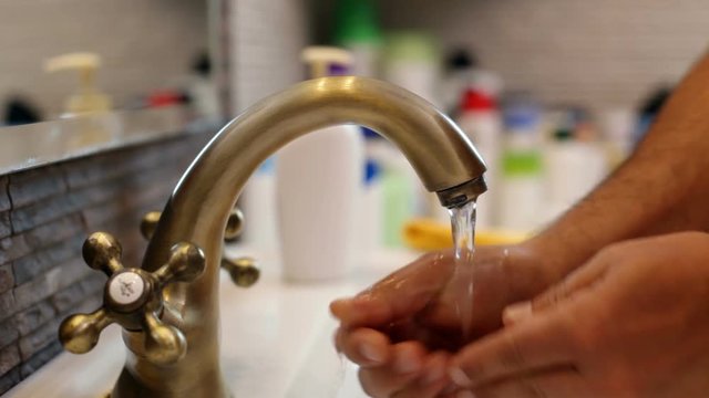 Man washing hands at the bathroom faucet, using towel - closeup, refocus