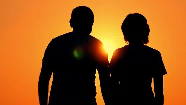 Silhouette of a happy couple. The guy hugs the girl against the sunset in a slow motion. Love of man and woman