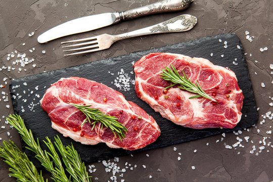 Steaks with herbs and spices on dark rustic background.