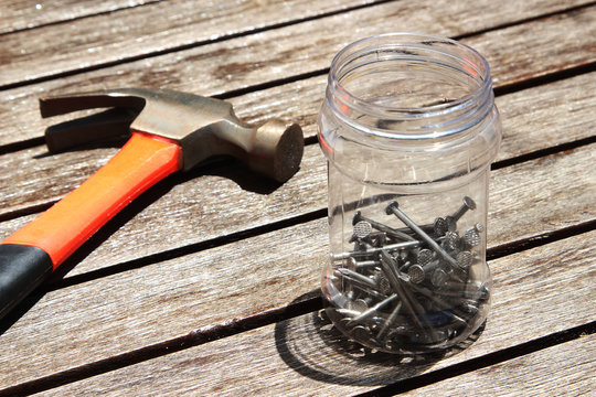 A hammer and a plastic jar of nails on a wooden table.  This image can be used to represent carpentry or DIY projects. 