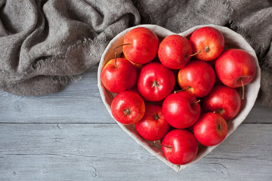Red apples, basket in the shape of heart on a wooden background