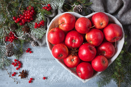 Red apples in a heart-shaped basket on a wooden background with Christmas tree branches and snow