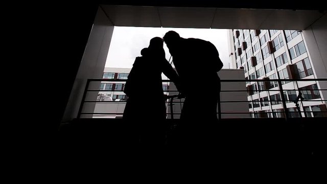 Rear view of lonely girl standing at balcony with bicycle. Silhouette of man and girl with bicycles. Silhouette of Lonely Woman with bicycle at balcony city background. Back view of young man