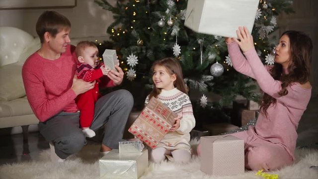 Happy family is giving presents to Christmas to each other. Mother is handing out beautiful boxes to her loving spouse and little cute children.