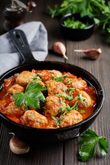 Meatballs in tomato sauce garlic and parsley in an iron frying pan on a dark brown wooden background. Selective focus.