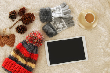 Cup of coffee next to tablet device with empty screen over cozy and warm fur carpet. Top view.