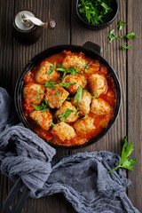Meatballs in tomato sauce garlic and parsley in an iron frying pan on a dark brown wooden background. Selective focus. Top view. Copy space.