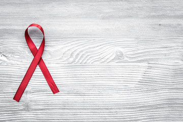 Red ribbon for HIV, AIDS, substance-abuse and anorexia awareness on grey wooden background top view copyspace