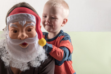 A happy child is holding a Santa Claus mask and an empty banner. Greeting card with Christmas. The concept of Christmas holidays