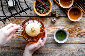 Pour tea from tea pot. Cups, dry tea leaves on rustic wooden background top view