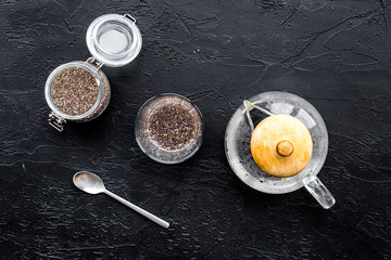Brew chia seeds. Jar with seeds, scoop, bowl, tea pot with hot water. Black background top view
