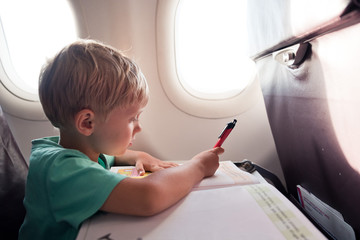 A 5 years old boy writing in the book while traveling by plane