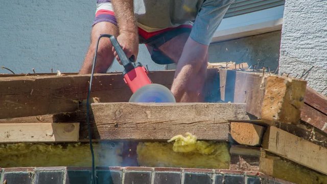 Man standing on jutting roof, cutting steel screws with special advanced angle grinder. Screw is really solid, puff of smoke is visible.