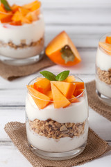 Persimmon creamy trifle in beautiful glasses, fresh ripe fruit slices on white wooden background. Healthy vegetarian food. Delicious dessert. Close up photography. Selective focus.