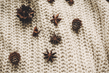 stylish christmas flat lay. pine cones anise on rustic knitted sweater background top view, space for text. atmospheric hygge winter image, seasonal greetings