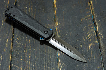 Black folding knife on black background. Wooden background.