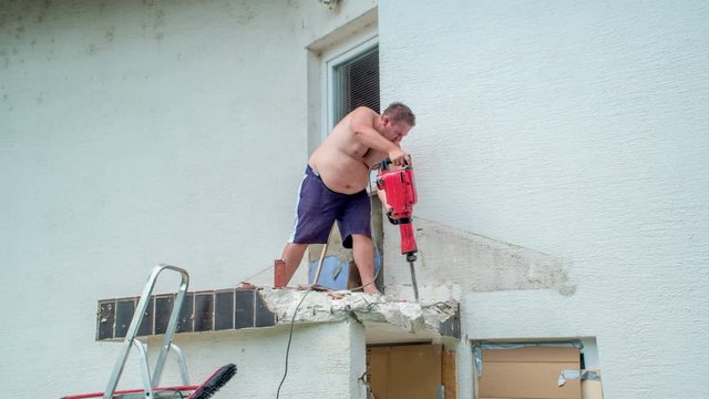 Young man demolishing solid concrete jutting roof with concrete demolition hammer.