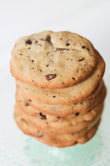 Stack of freshly baked, homemade  traditional American Chocolate Chip Cookies on glass cake stand on white background