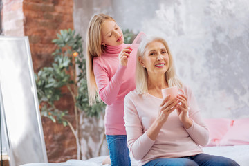Pleasurable rest. Happy nice aged woman holding a cup of tea and enjoying her rest while waiting for a new hairstyle to be made