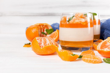 Creamy panna cotta with orange jelly in beautiful glasses, fresh ripe mandarin, blue textile on...