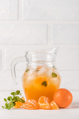 Mandarin cocktail with ice and mint in beautiful glasses and jug, fresh ripe citrus on white wooden background. Sweet orange juice. Close up photography. Selective focus