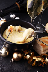 Gourmet Swiss fondue dinner on a winter evening alongside a heated pot of cheese fondue with two forks dipping bread and champagne