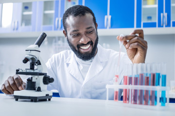 For analysis. Cheerful nice positive scientist in front of the microscope and taking a sample of liquid while doing biological analysis