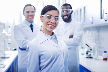 Ready to work. Nice positive young woman standing with her scientist team and smiling while being ready to work