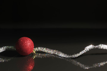 Black reflective tabletop with red christmas ornament and tinsel tabletop